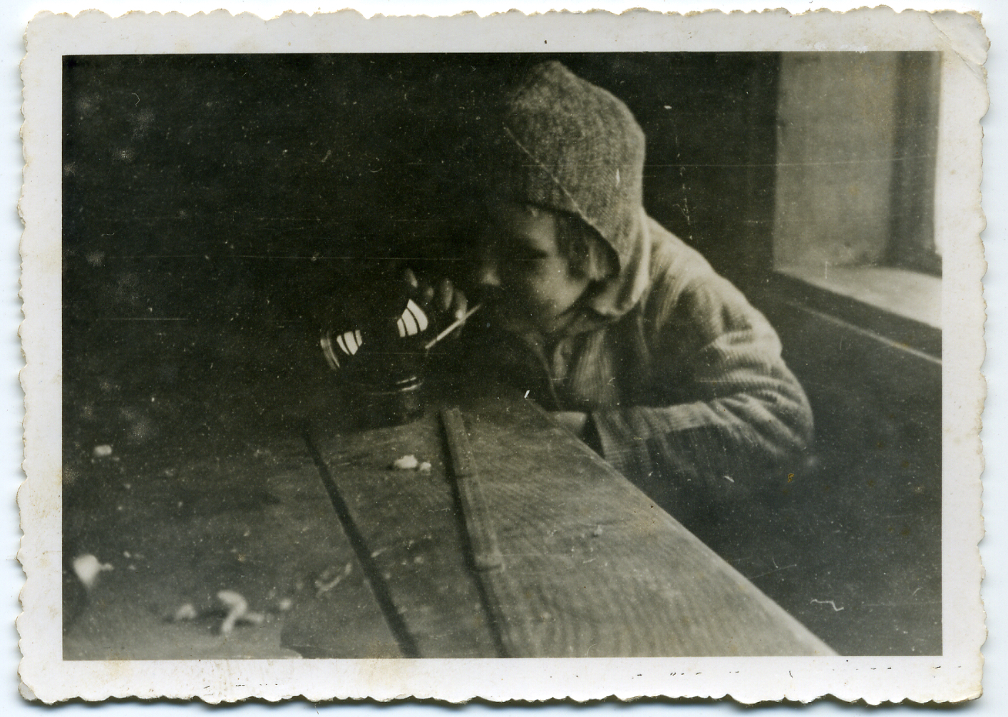 Stara wyblakła fotografia przedstawia chłopczyka, który przegląda się w szklanej kuli, ustawionej na stole. W ustach ma cienką rurkę, którą trzyma palcami, jakby palił papierosa.