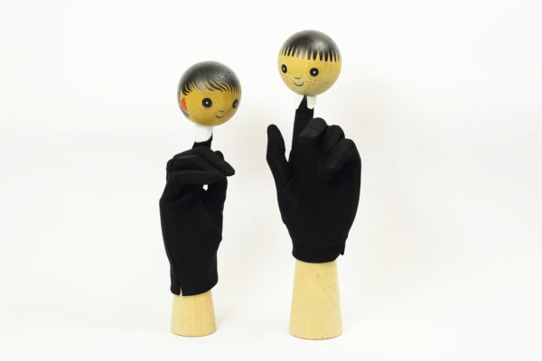 Dwie czarne rękawiczki maja umieszczone na palcu wskazującym, dwie okrągłe głowy lalek.