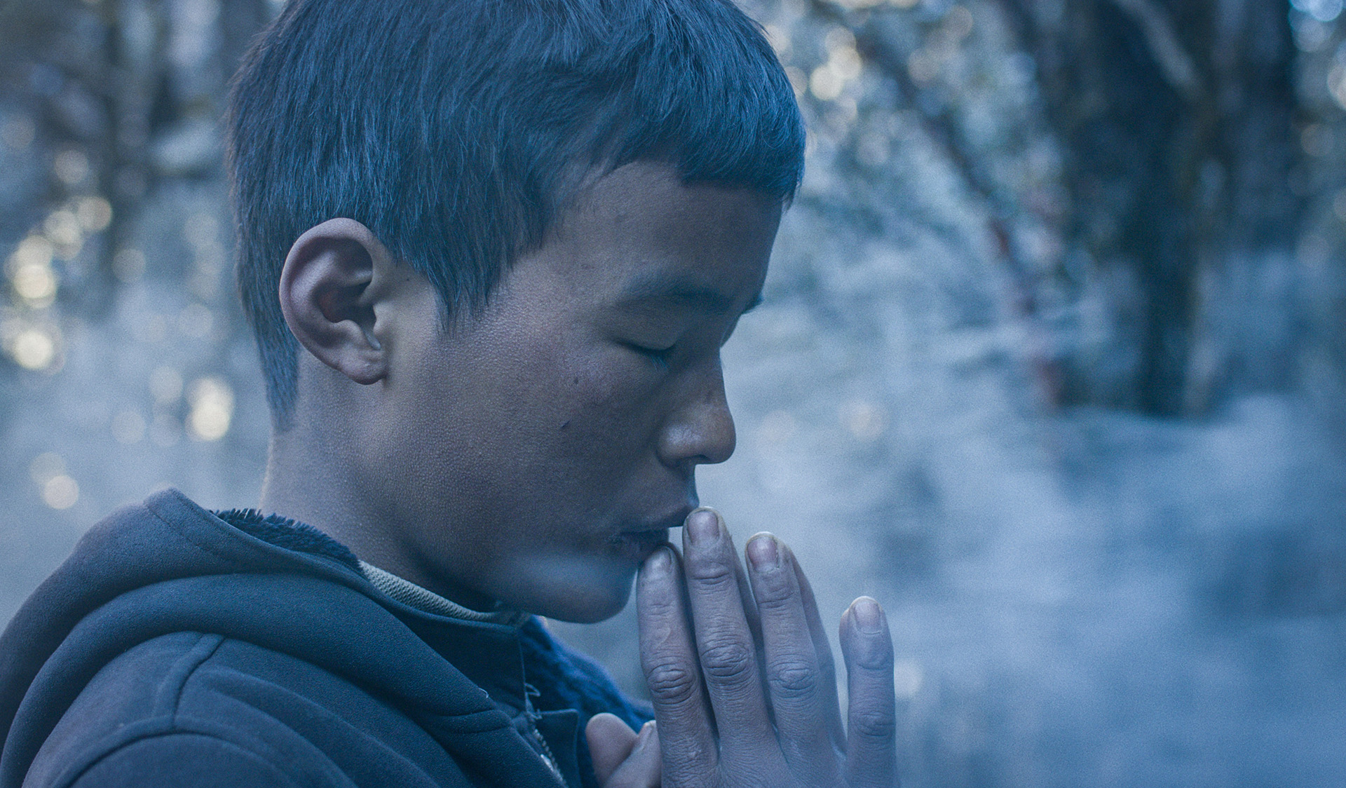 Chłopiec modli się z zamkniętymi oczami. Jego złożone dłonie dotykają jego ust.