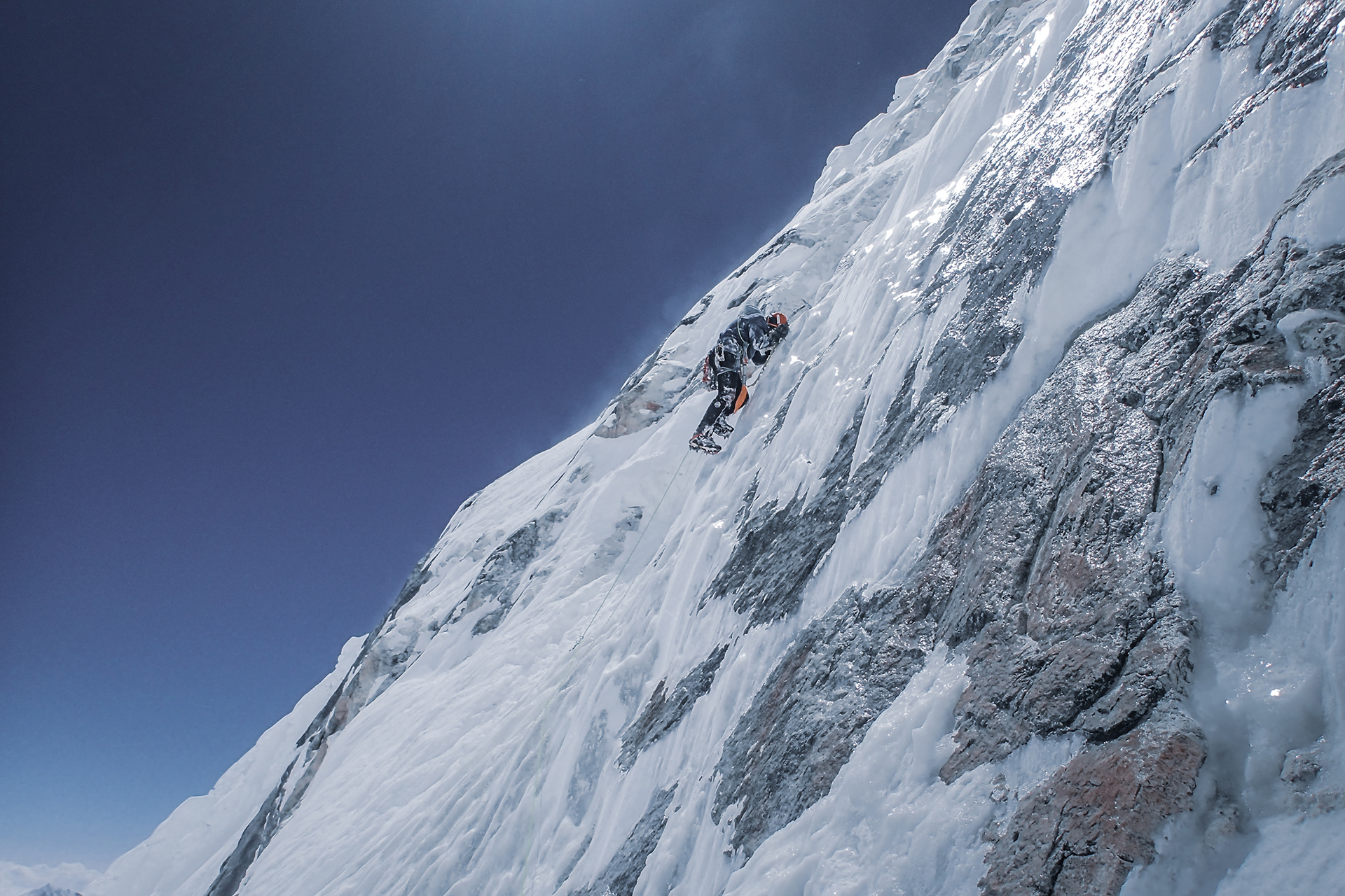 Człowiek wspina się po prawie pionowej ścianie szczytu, w większości pokrytej lodem.