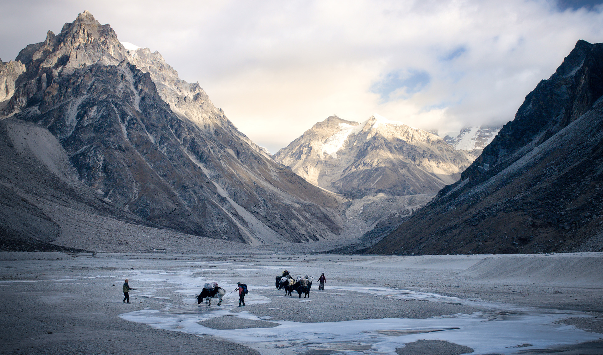 Grupa ludzi wraz z osłami trzymającymi na plecach ich dobytek, przeprawiają się przez przełęcz.