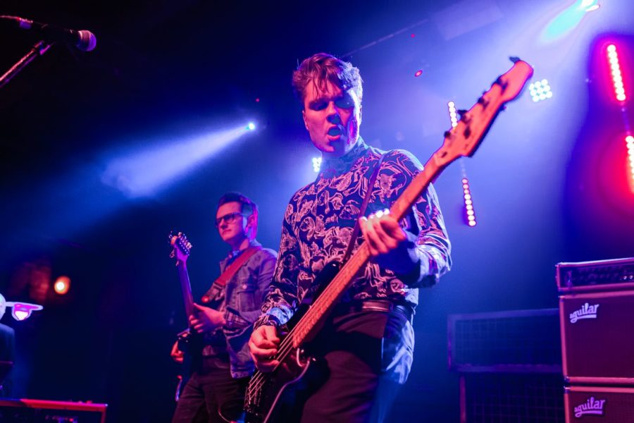 Na pierwszym planie Stefan Nowakowski daje koncert na gitarze basowej, na drugim planie Łukasz Borowicki gra na gitarze elektrycznej.