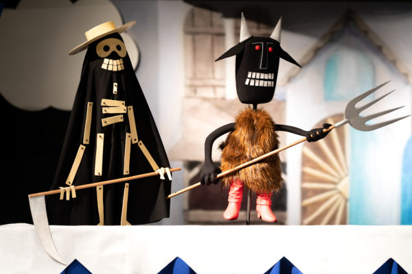 Dwie lalki na scenie, ustawione profilem. Lalka po lewej przedstawia śmierć, po prawej – diabła.