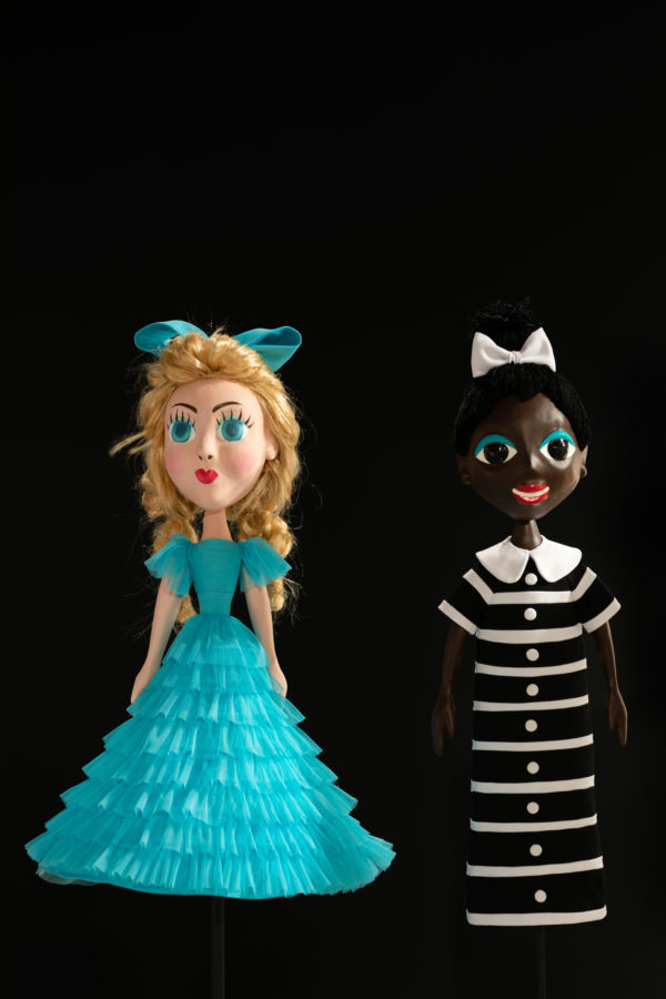 Dwie lalki ustawione frontem, przymocowane prętem do podłogi. Po lewej lalka wygląda jak księżniczka, po prawej lalka w stroju służki.