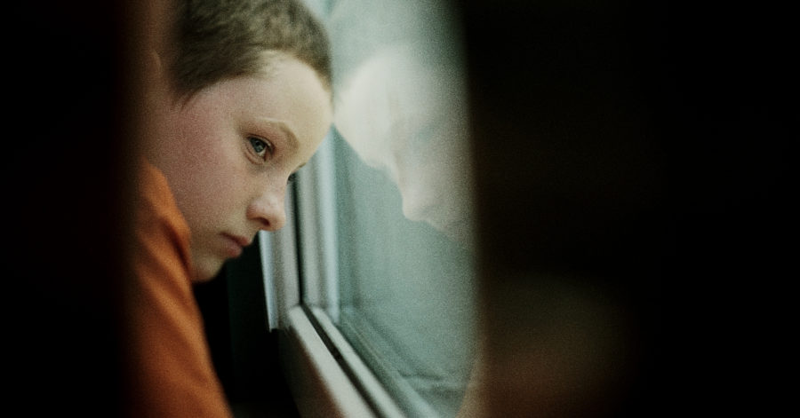 Chłopczyk nostalgicznie patrzy przez okno. W szybie odbija się jego twarz.