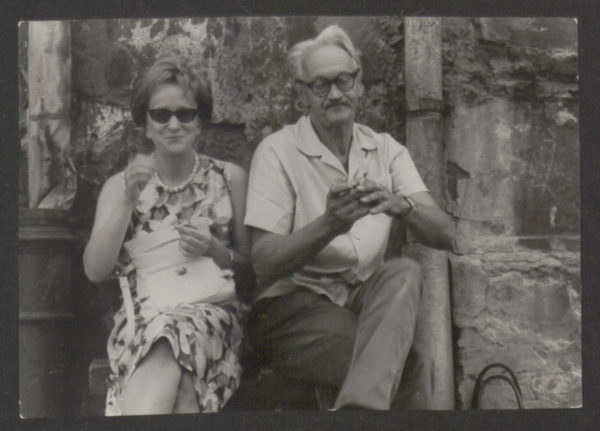 Wiesława Szymborska siedzi na ławce obok starszego mężczyzny, który pali papierosa.