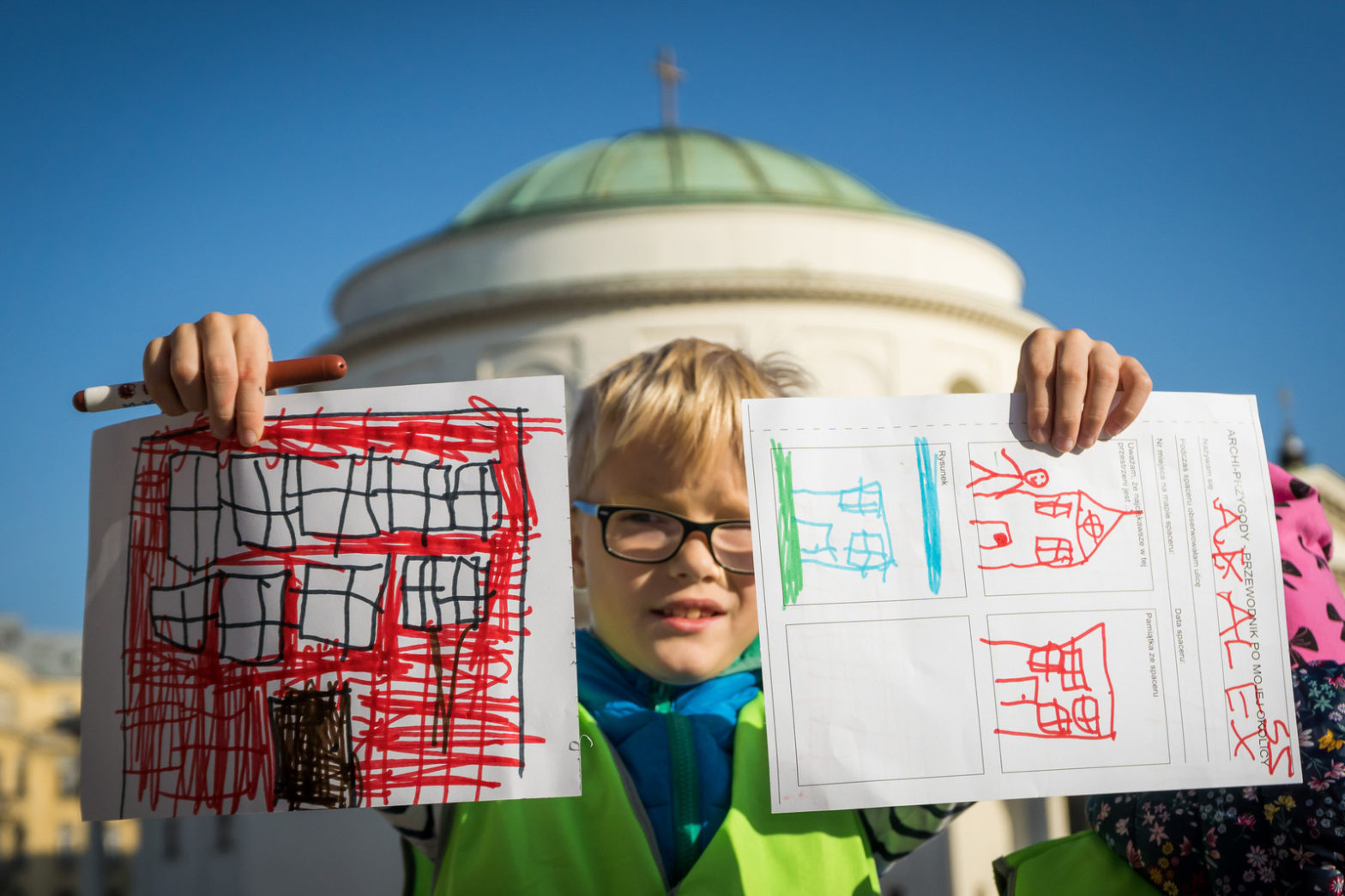 Dziecko pokazuje swoje kolorowe rysunki budynków.