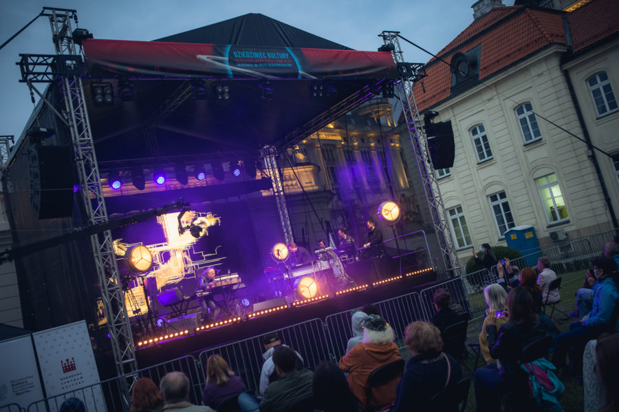 Publiczność słucha koncertu, który odbywa się na scenie.